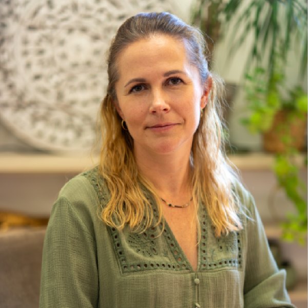 Kobieta w długich włosach uśmiecha się. Ma zieloną bluzę, w tle kwiaty.