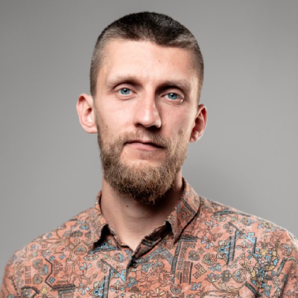 Mężczyzna w kropkowanej koszuli trzyma się za brodę.