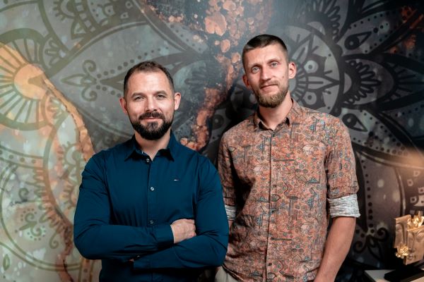 Dwójka uśmiechniętych mężczyzn. W tle kolorowa ściana.