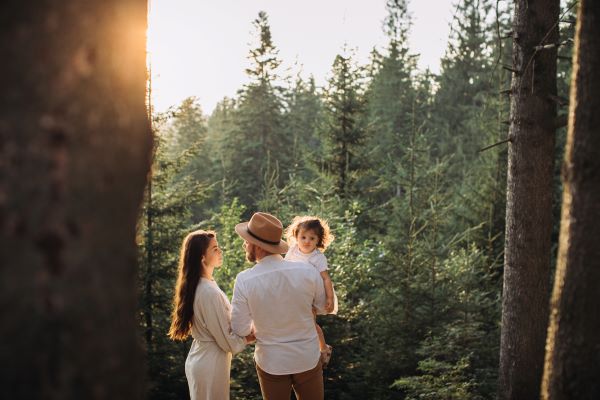 Rodzina w lesie. Facet trzyma dziecko na rękach, po lewej kobieta. W tle las.