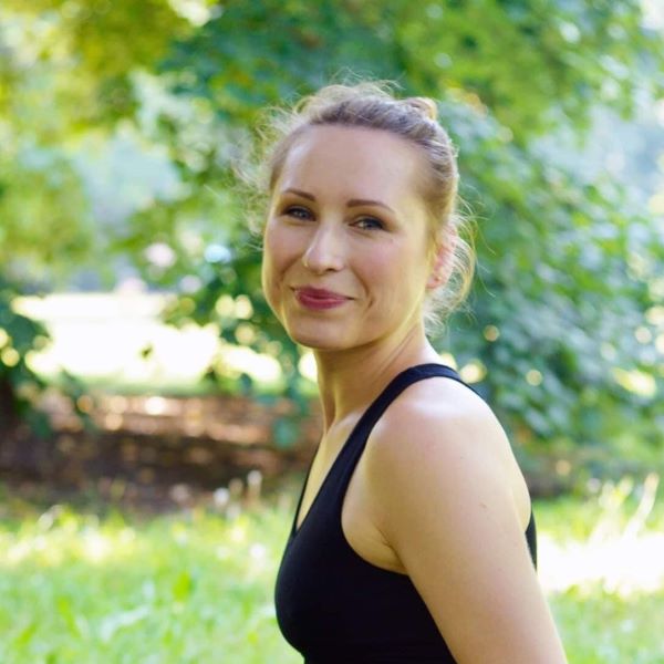 Uśmiechnięta kobieta w czarnej bluzce. W tle drzewa. Zielona atmosfera.