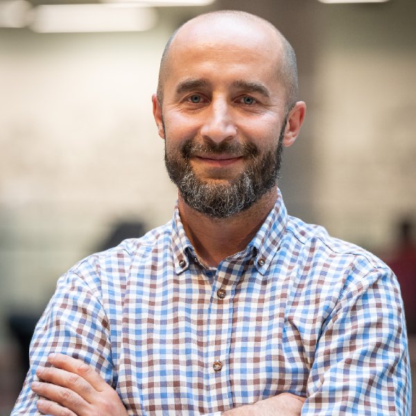 Uśmiechnięty, łysy mężczyzna z brodą w koszuli w kolorowe kwadraty.